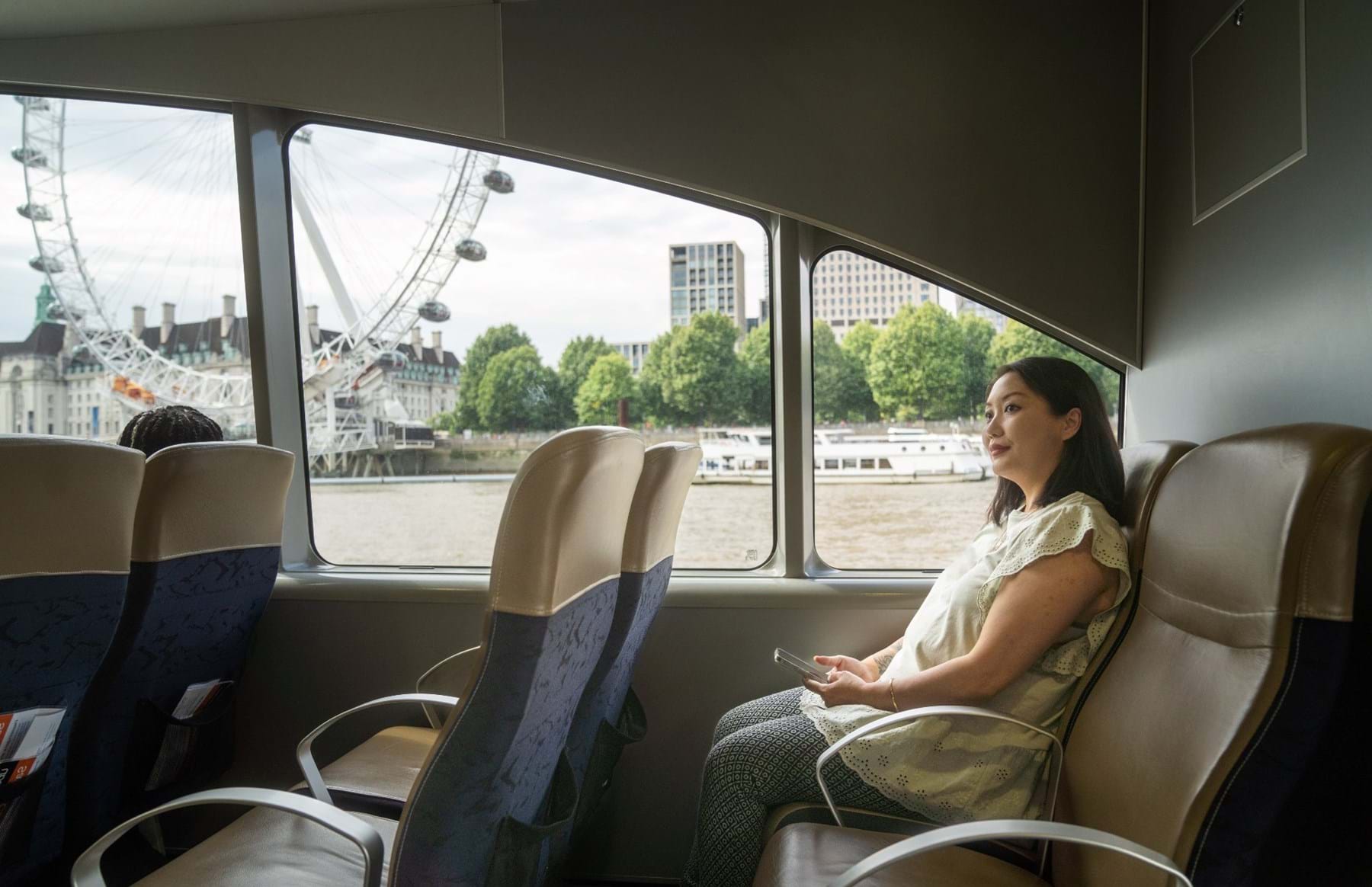 Woman sitting inside the River Bus with London Eye through the window